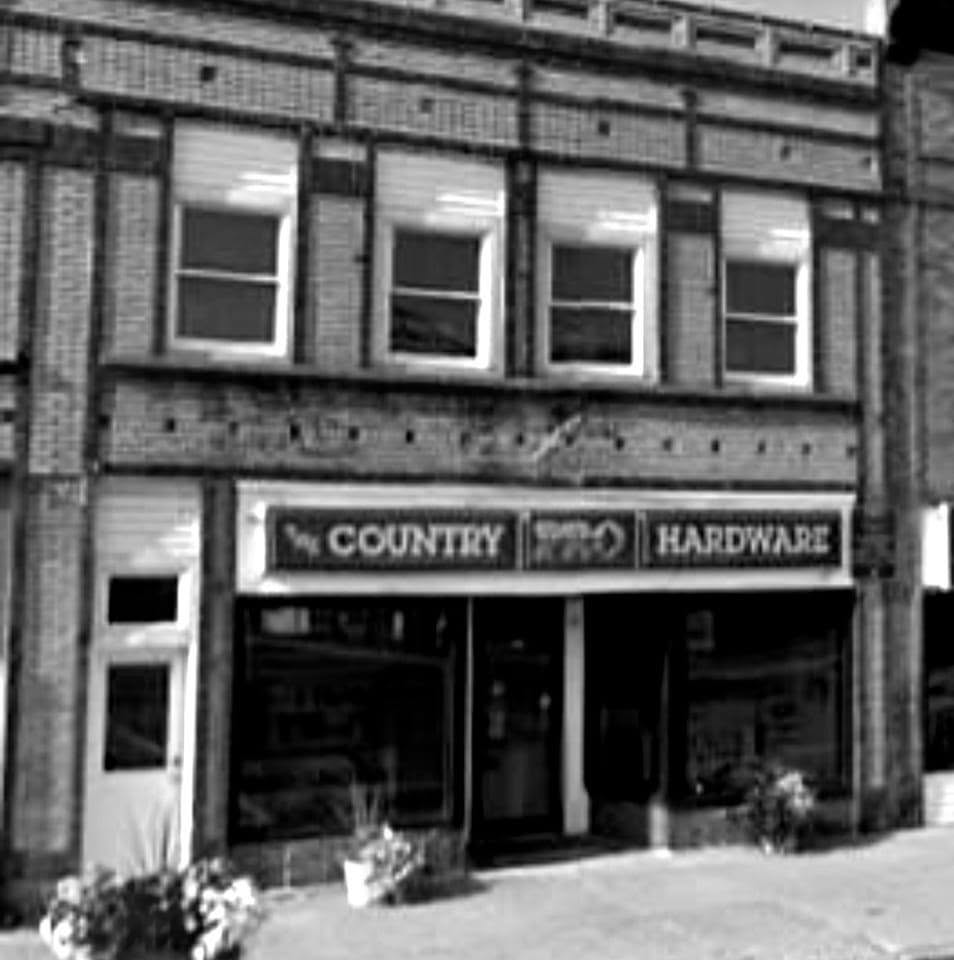 Black and white photograph of a brick building storefront with a sign reading 'The Country Hardware'.