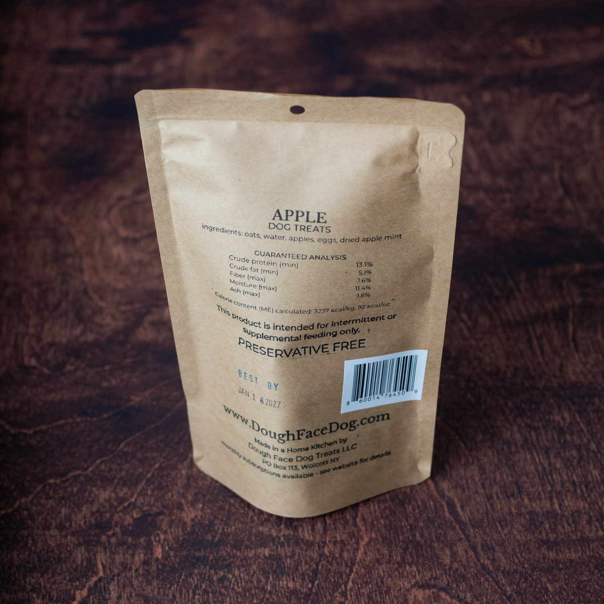Back informational panel of a brown kraft paper stand up pouch of Dough Face Dog Treats apple flavored dog treats, on a brown wooden textured background.