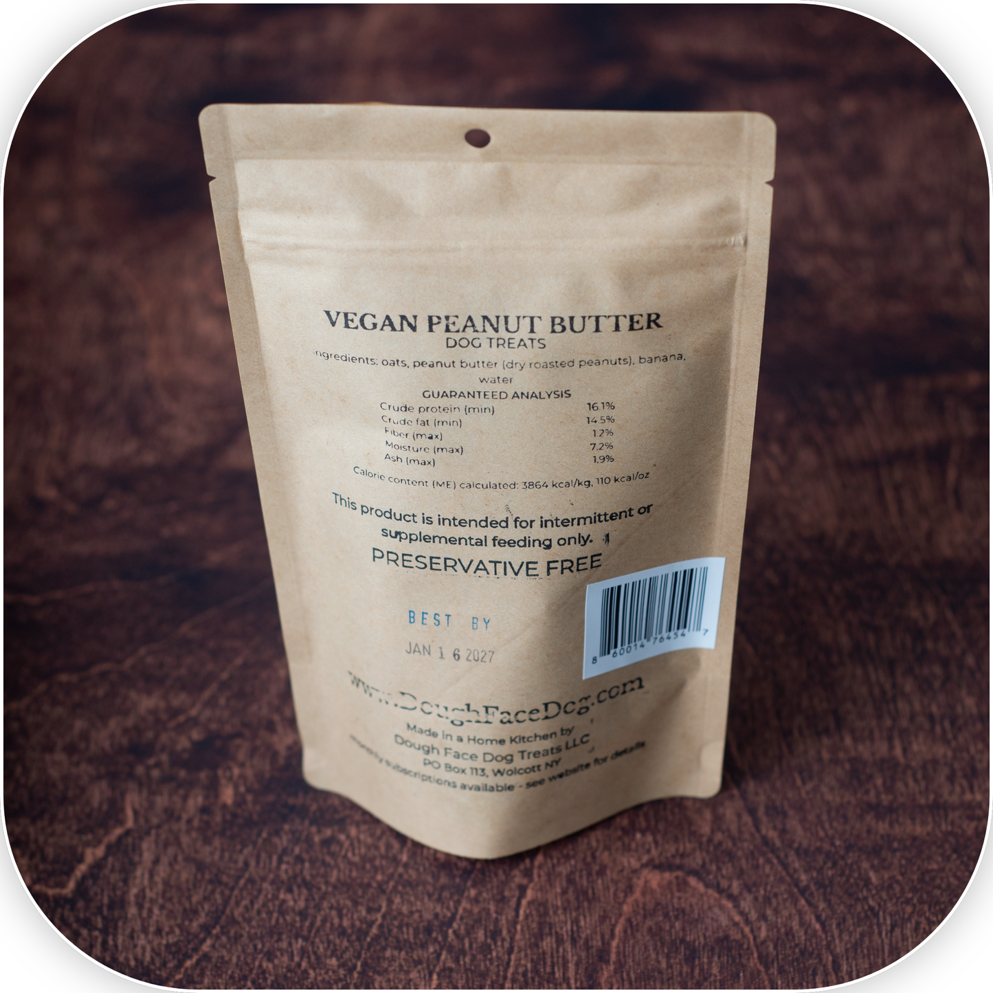 A stand-up pouch of Dough Face Dog Treats Vegan Peanut Butter dog treats, shown from the back on a dark brown textured background.