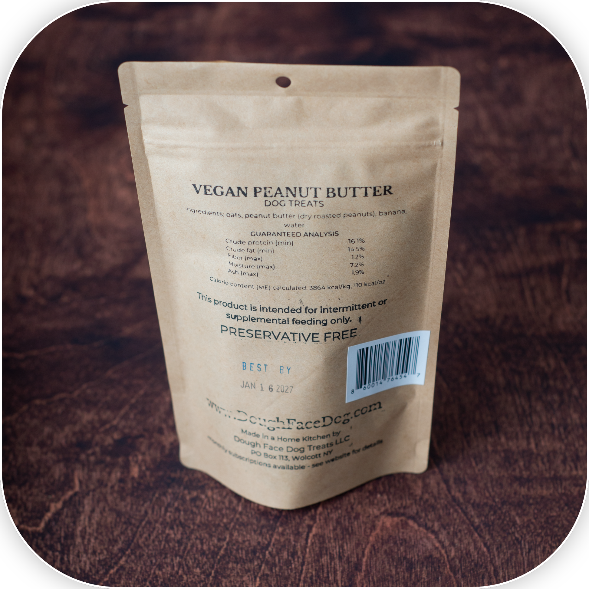 A stand-up pouch of Dough Face Dog Treats Vegan Peanut Butter dog treats, shown from the back on a dark brown textured background.