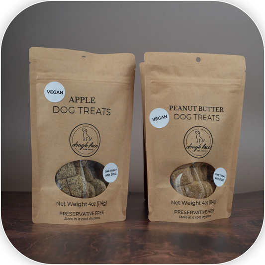 Two stand-up kraft paper pouches of dog treats on a dark wooden surface against a gray background. The left pouch is labeled Apple Dog Treats, and the right pouch is labeled Peanut Butter Dog Treats.