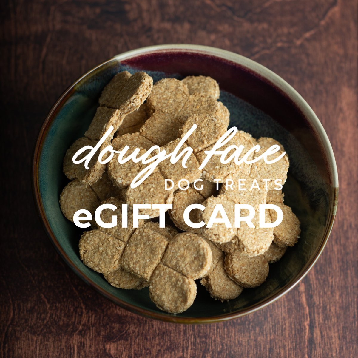 A top-down view of a ceramic bowl filled with round dog treat pieces on a dark wooden surface, with large white text reading 'dough face DOG TREATS eGIFT CARD' overlaid across the center.