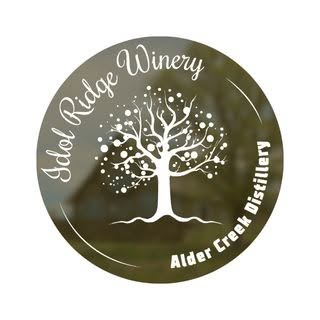 A circular logo with a white tree in the center and the words "Idol Ridge Winery" in cursive around the top left and "Alder Creek Distillery" around the bottom right.