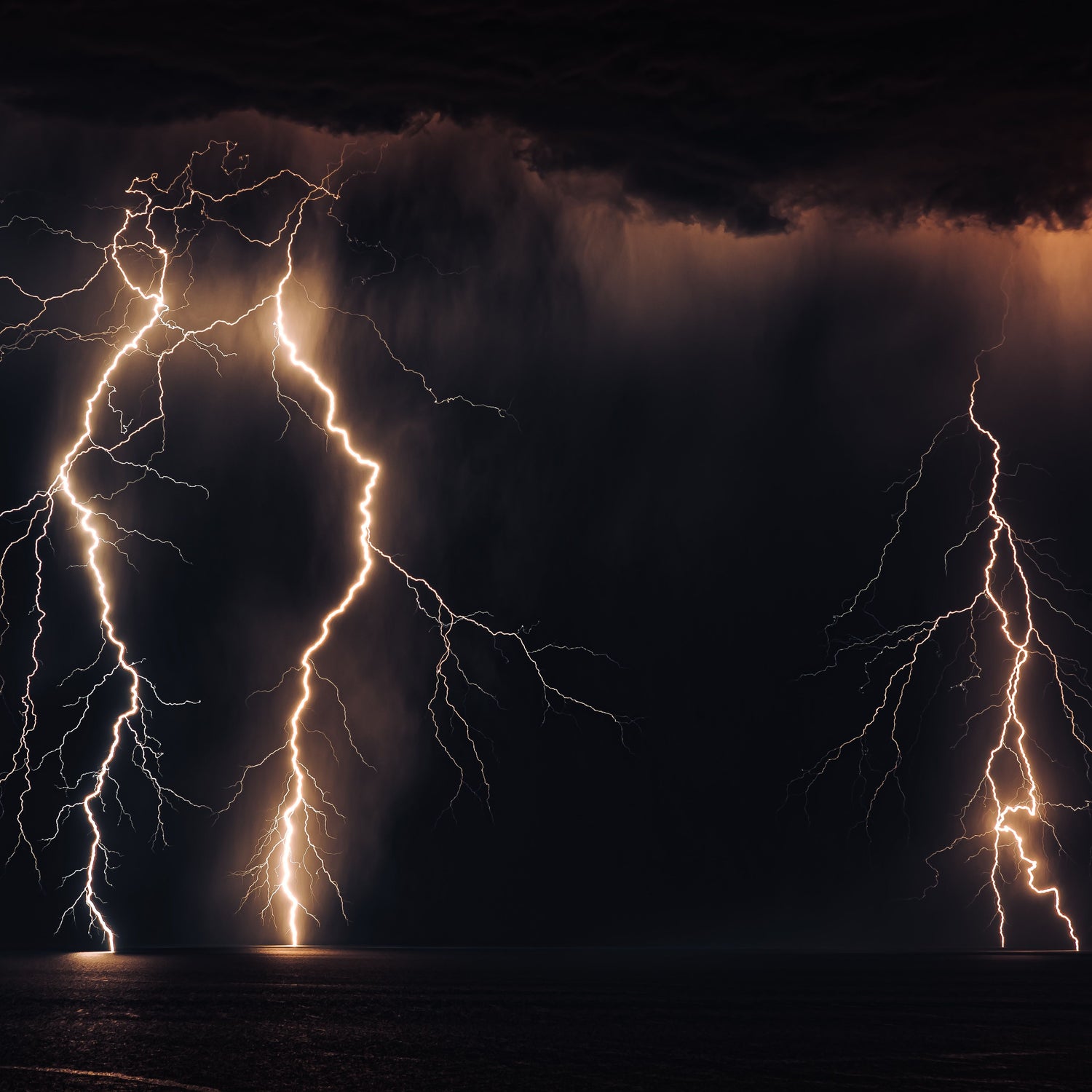 A dramatic storm scene with multiple bright lightning strikes in a dark night sky above a reflective dark surface, with warm orange light filtering through the clouds.