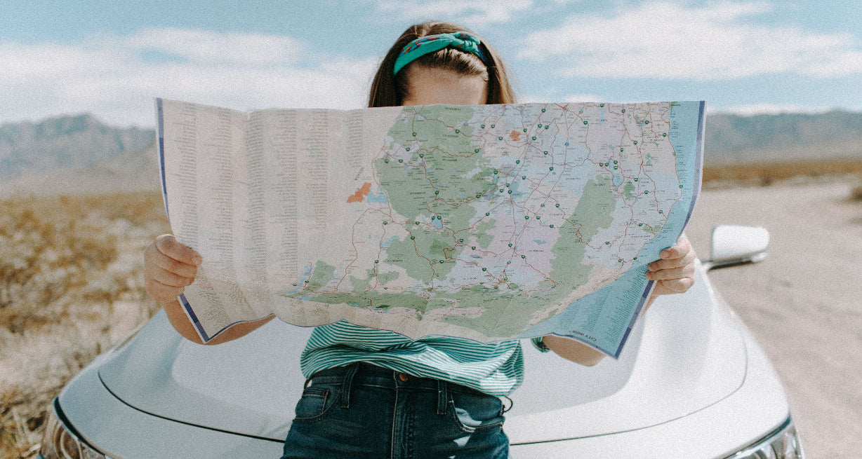 Person holding a world map in front of a car in a desert setting