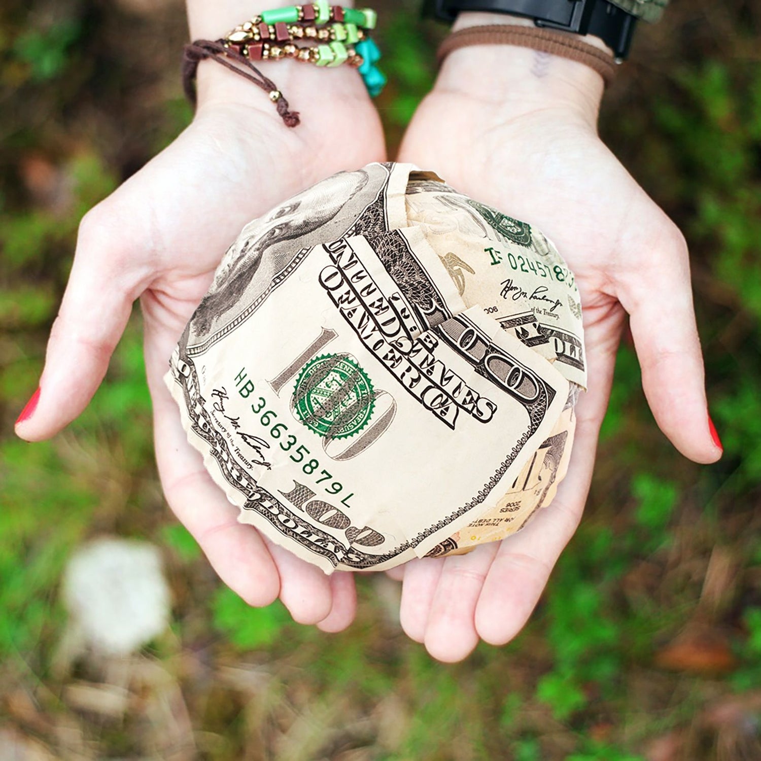 A pair of hands holding a ball made from a U.S. dollar bills, a $100 bill on the outside.