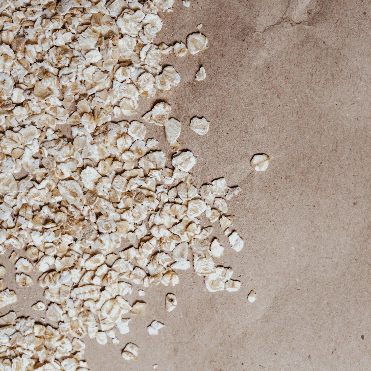 Rolled oats scattered on a brown kraft paper background.