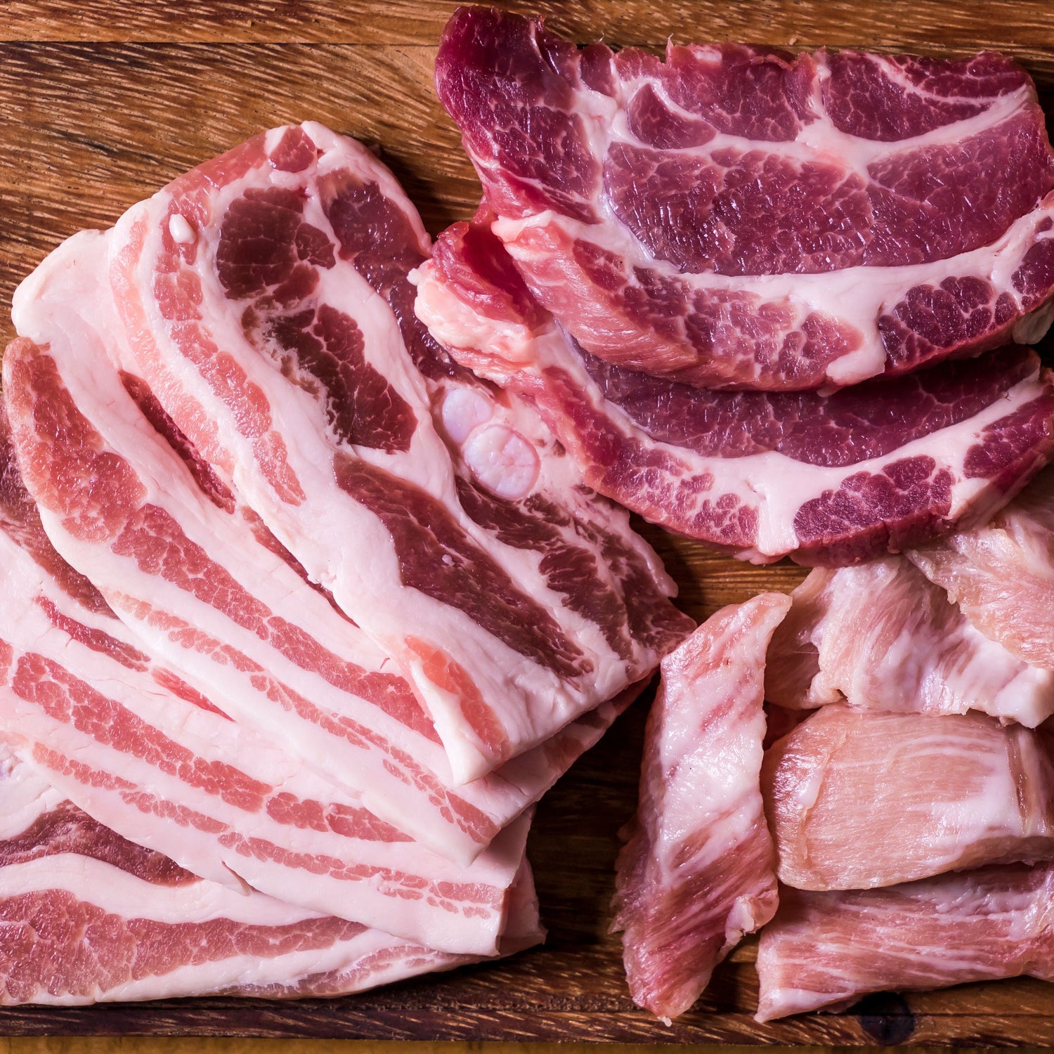 Raw meat slices on a wooden cutting board with vegetables
