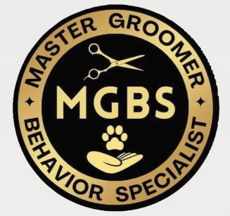 A circular black and gold badge or emblem with the text 'MASTER GROOMER BEHAVIOR SPECIALIST' around the border, 'MGBS' in the center, a pair of scissors at the top, and a paw print with an open hand at the bottom.