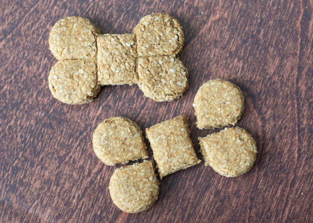 Two bone-shaped dog treats with a textured oat surface, arranged on a dark brown wooden background.