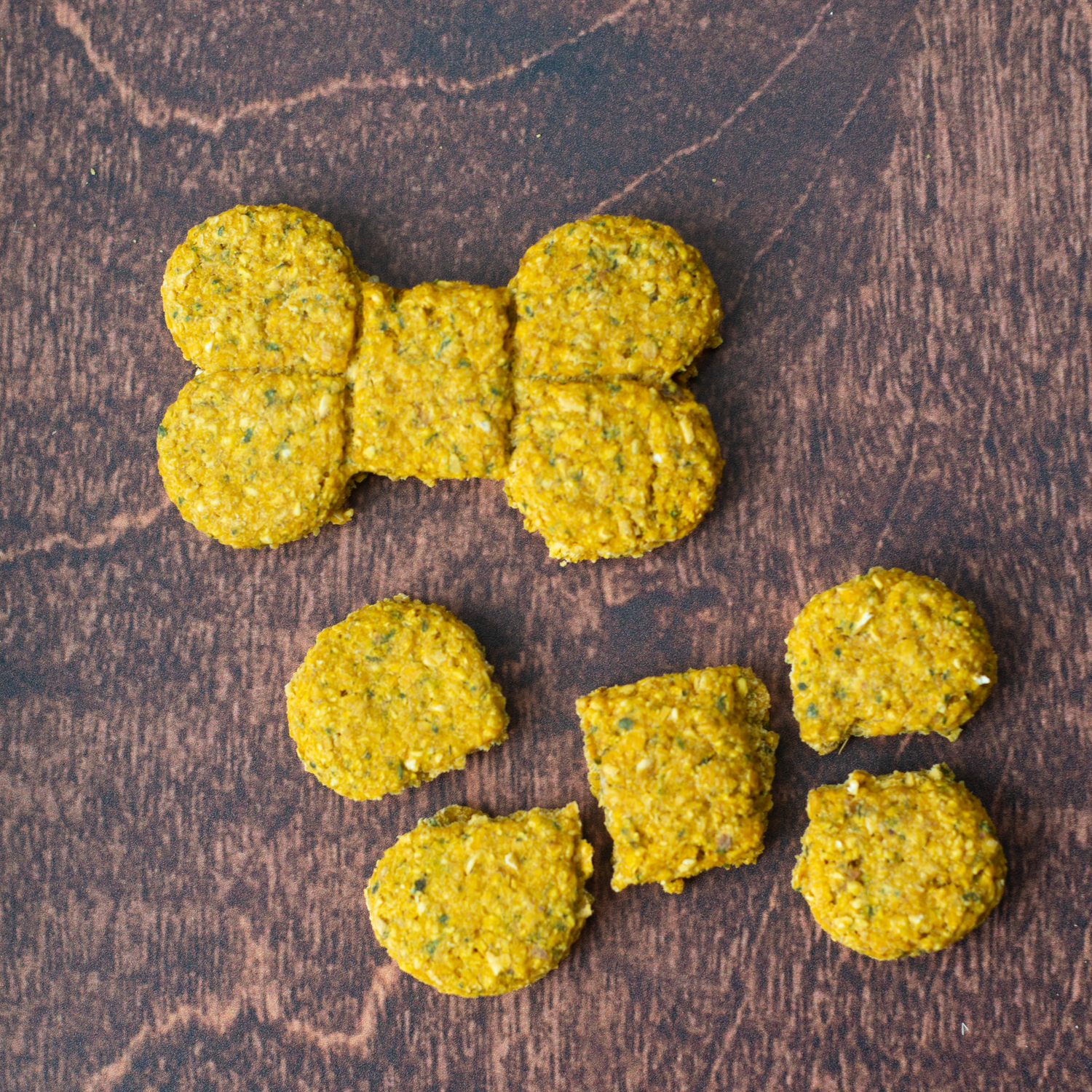 Sweet Potato dog treats shaped like a bone and several small round pieces arranged on a dark brown wooden surface.